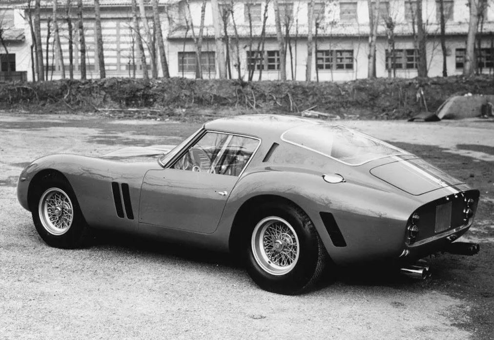 Ferrari 250 GTO de 1962 photographiée en noir et blanc, vue de trois quarts arrière avec ses ailes galbées et ses roues à rayons.