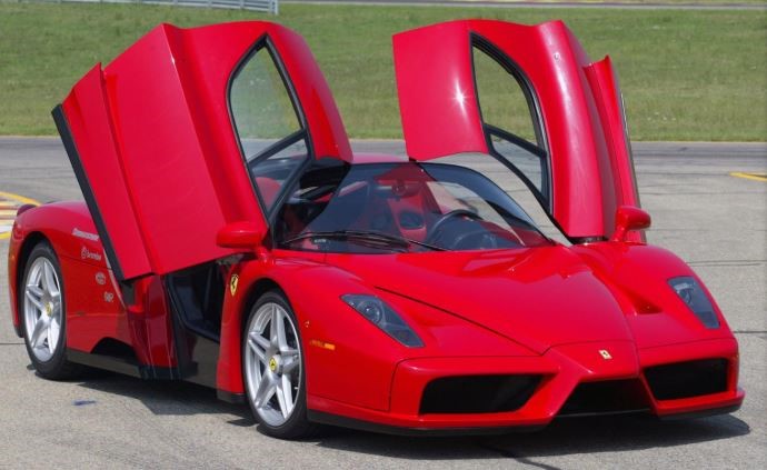 Ferrari Enzo rouge avec ses deux portes ouvertes vers le haut, vue de trois quarts avant.