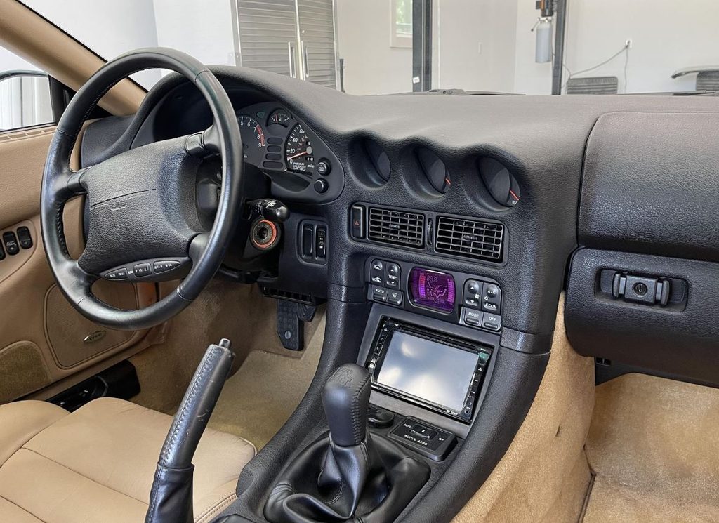Intérieur de la Mitsubishi 3000 GT VR-4 avec tableau de bord orienté vers le conducteur, trois cadrans centraux et boîte manuelle.