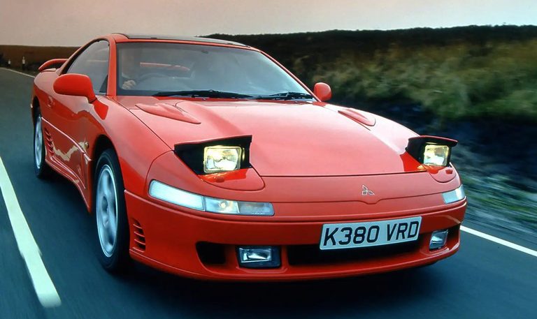 Mitsubishi 3000 GT rouge de première génération roulant avec ses phares escamotables relevés.