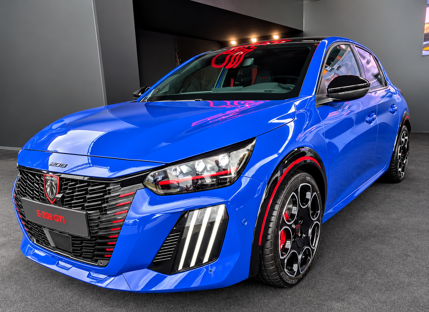 Peugeot E-208 GTi bleue vue de trois quarts avant avec jantes sportives et détails rouges