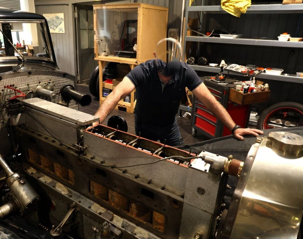 Immense moteur huit cylindres de Bugatti Royale en cours de restauration, avec un mécanicien à ses côtés.