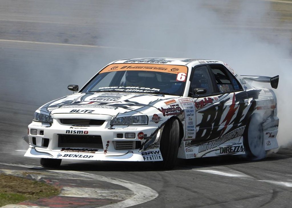 Nissan Skyline R34 de compétition en pleine dérive sur circuit, roues avant en contre-braquage et pneus arrière fumants.