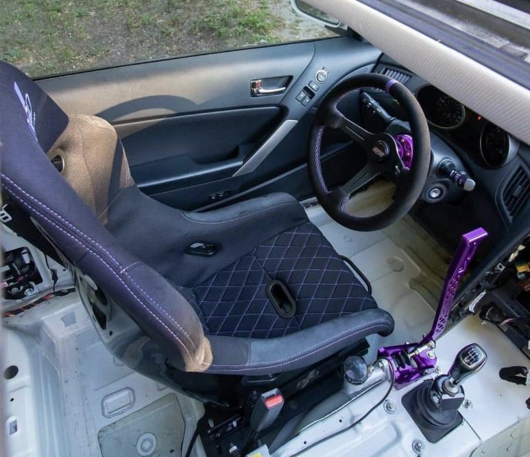 Habitacle d'une voiture préparée pour le drift avec siège baquet, volant sport et grand levier de frein à main hydraulique violet.