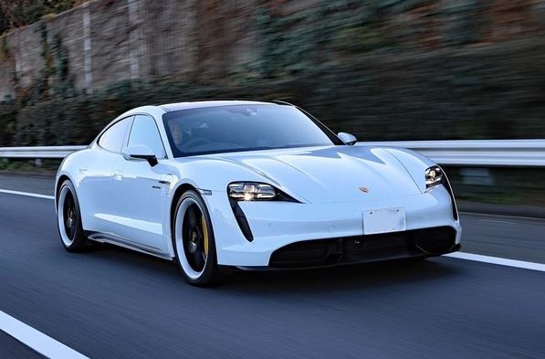 Porsche Taycan blanche photographiée en mouvement sur une route, berline sportive électrique de la marque.