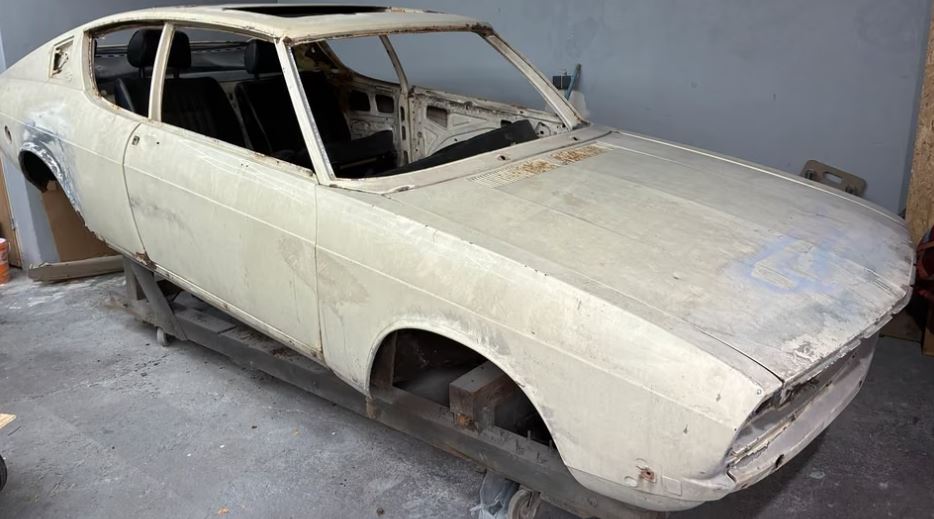 Audi 100 Coupé S de 1975, carrosserie blanche démontée et dépourvue de vitrages et de roues, en attente de restauration.