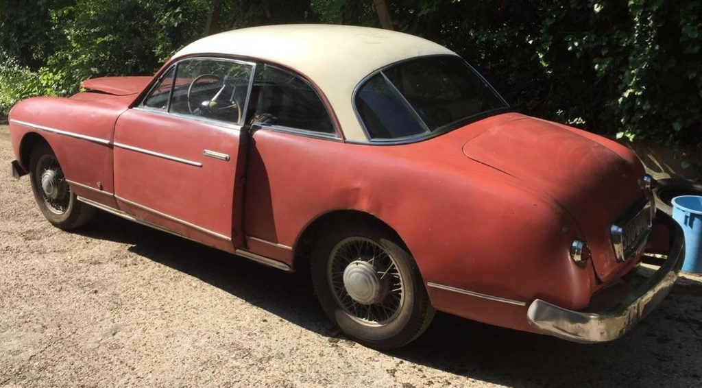 Ford Comète V8 Monte Carlo de 1954, carrosserie rouge et toit clair, retrouvée dans son état ancien avec une portière entrouverte.