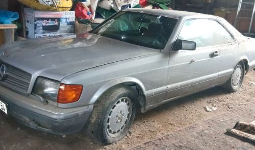 Mercedes 560 SEC de 1990 grise immobilisée dans un garage, en attente d'une remise en état