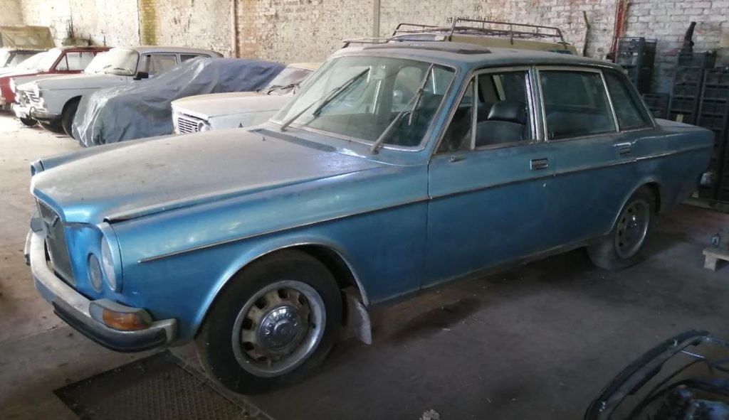Volvo 164 de 1973 bleue, abandonnée dans un ancien garage, avec carrosserie poussiéreuse et galerie de toit.