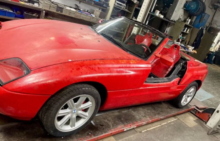 BMW Z1 rouge de 1989 dans un atelier, peinture défraîchie et porte escamotable abaissée dans le bas de caisse.