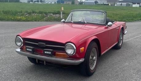 Triumph TR6 rouge de 1972, roadster britannique ancien photographié de trois quarts avant, capote ouverte.