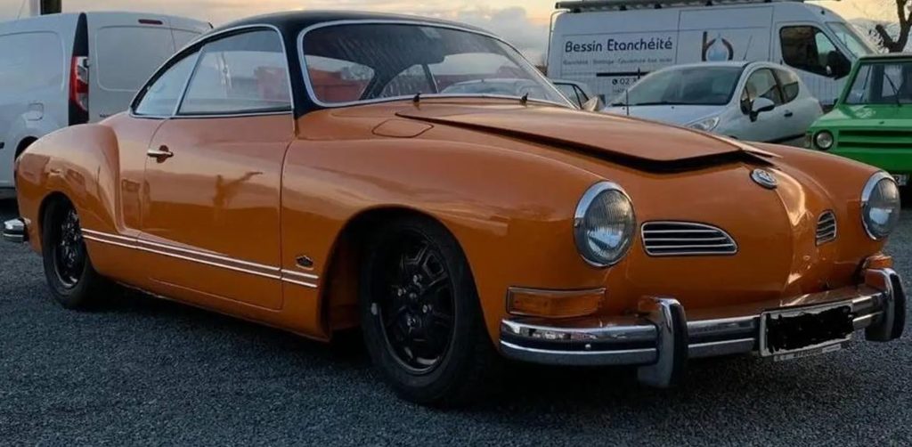 Volkswagen Karmann Ghia coupé de 1971 orange avec toit noir, capot avant entrouvert et jantes noires.