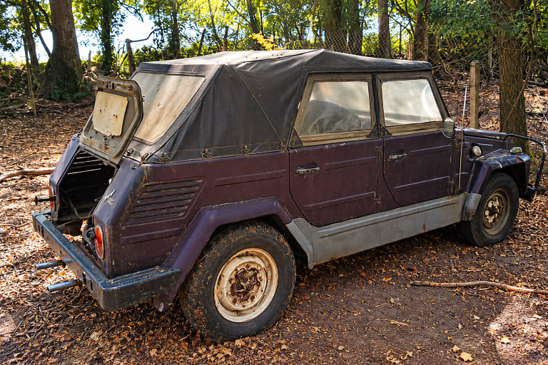 Volkswagen 181 de 1971 abandonnée sous les arbres, avec capote en toile vieillissante, carrosserie poussiéreuse et hayon arrière ouvert.