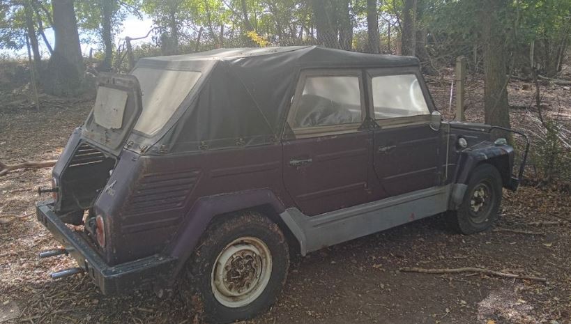Volkswagen 181 de 1971 abandonnée sous les arbres, avec capote en toile vieillissante, carrosserie poussiéreuse et hayon arrière ouvert.