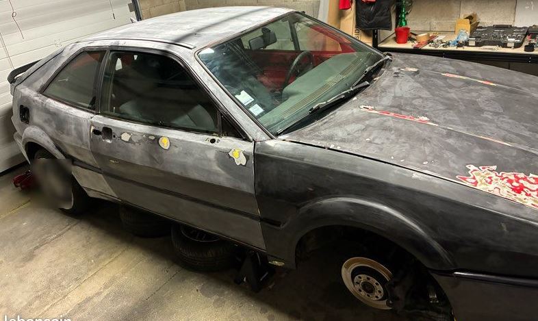 Volkswagen Corrado G60 de 1990 en cours de restauration, carrosserie partiellement poncée et roues démontées dans un garage.