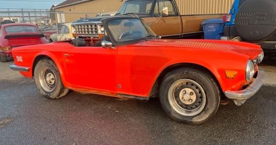 Triumph TR6 de 1973 rouge, capote repliée, photographiée de profil avec ses jantes en acier et ses chromes.