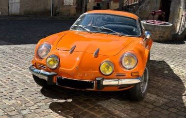 Alpine A110 V85 de 1975 orange, photographiée de trois quarts avant dans une cour pavée.