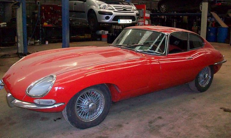 Jaguar Type E de 1961 rouge, première série à plancher plat, photographiée de trois quarts avant dans un garage.