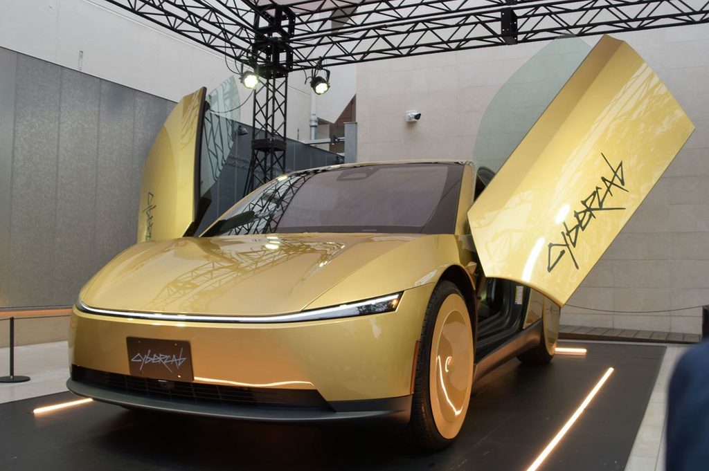 Tesla Cybercab doré présenté de trois quarts avant, avec ses deux portes papillon ouvertes.