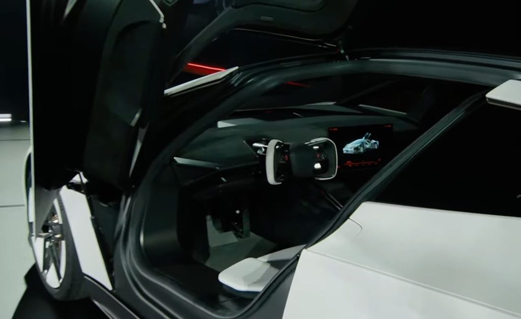 Intérieur du nouveau Tesla Roadster 2026 avec volant rectangulaire, écran central et porte relevée.