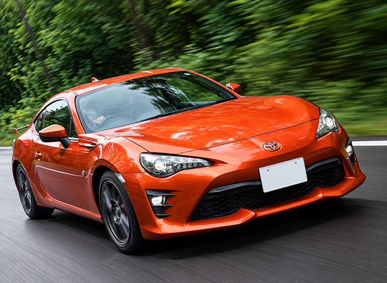Toyota GT86 orange photographiée de trois quarts avant sur route, coupé sportif japonais à moteur Boxer Subaru.