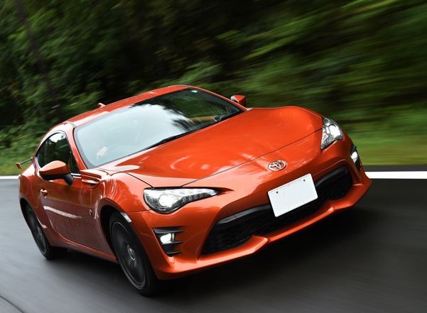 Toyota GT86 orange photographiée de trois quarts avant sur route, coupé sportif japonais à moteur Boxer Subaru.