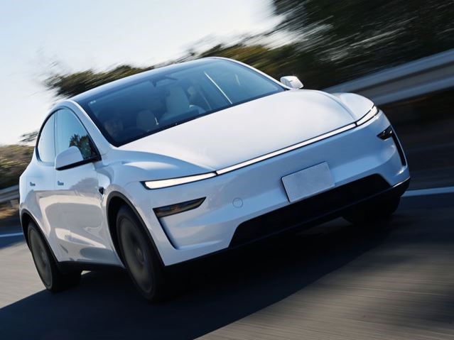 Tesla Model Y blanche photographiée de trois quarts avant en circulation sur une route.