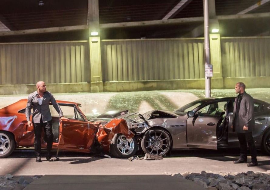 Jason Statham dans une scène de Fast & Furious 7, face à une voiture accidentée.